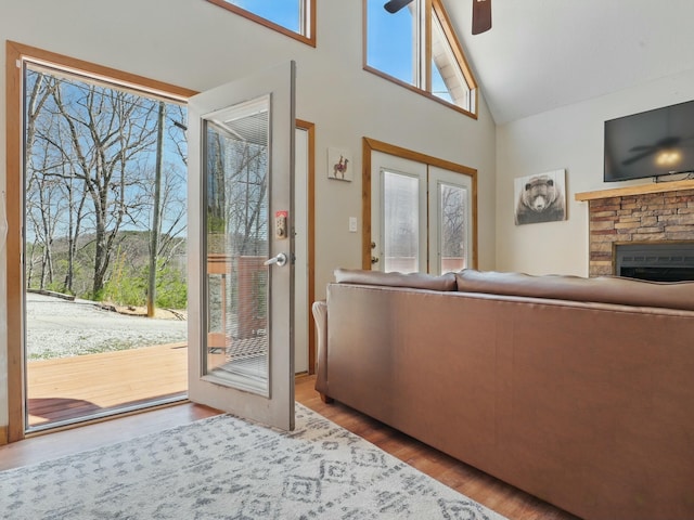 unfurnished living room with a stone fireplace, high vaulted ceiling, wood finished floors, and ceiling fan