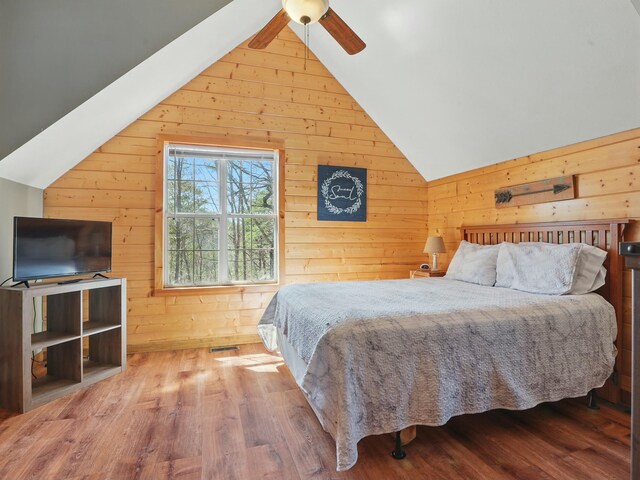 bedroom with vaulted ceiling, wooden walls, and wood finished floors