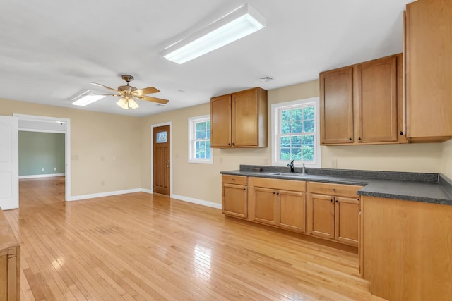 kitchen featuring dark countertops, light wood finished floors, baseboards, ceiling fan, and a sink