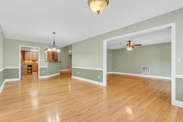 unfurnished room with baseboards, ceiling fan with notable chandelier, visible vents, and light wood-type flooring