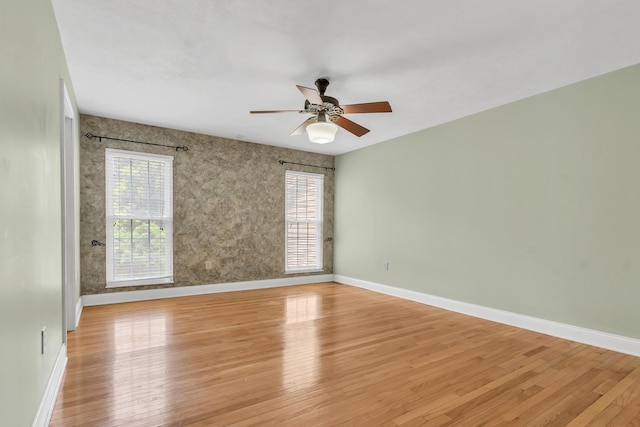 spare room featuring light wood-style flooring, a ceiling fan, and baseboards