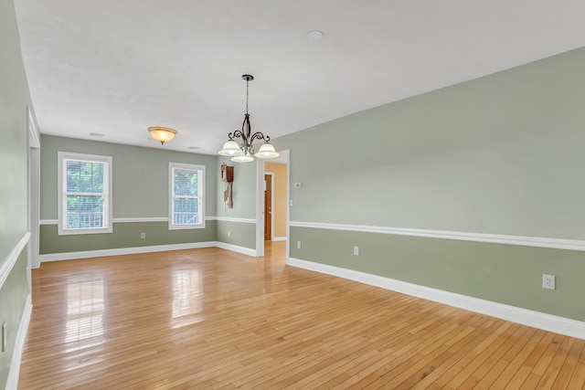 spare room with baseboards, light wood-style floors, and an inviting chandelier