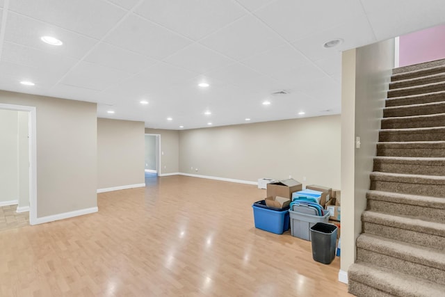 finished below grade area featuring light wood finished floors, stairway, recessed lighting, and baseboards