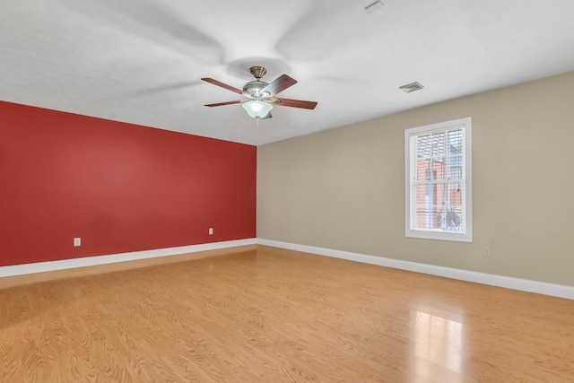 spare room featuring visible vents, light wood-style flooring, a ceiling fan, and baseboards