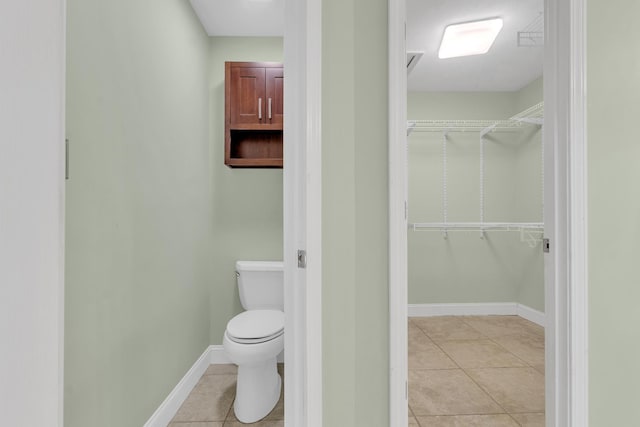 bathroom with tile patterned flooring, a walk in closet, toilet, and baseboards