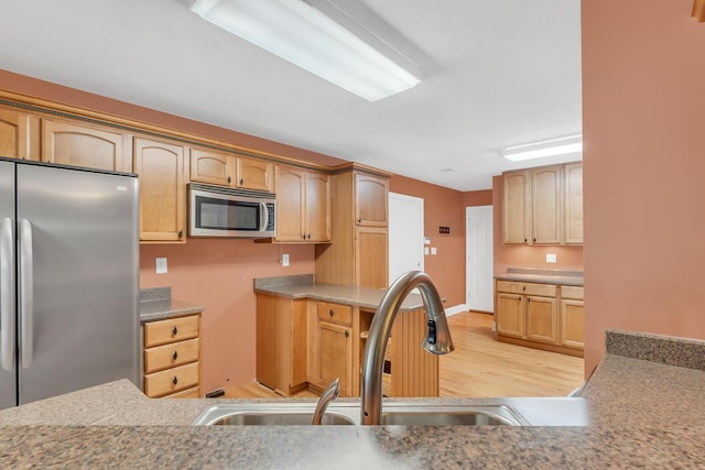 kitchen featuring light wood-style flooring, light brown cabinetry, a sink, appliances with stainless steel finishes, and light countertops