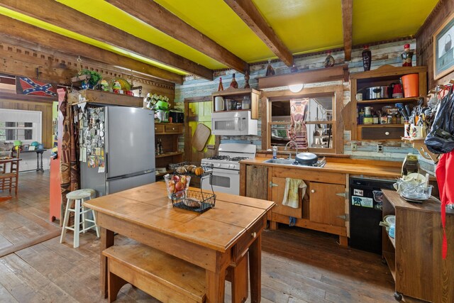 kitchen featuring white appliances, sink, wooden walls, hardwood / wood-style flooring, and beam ceiling