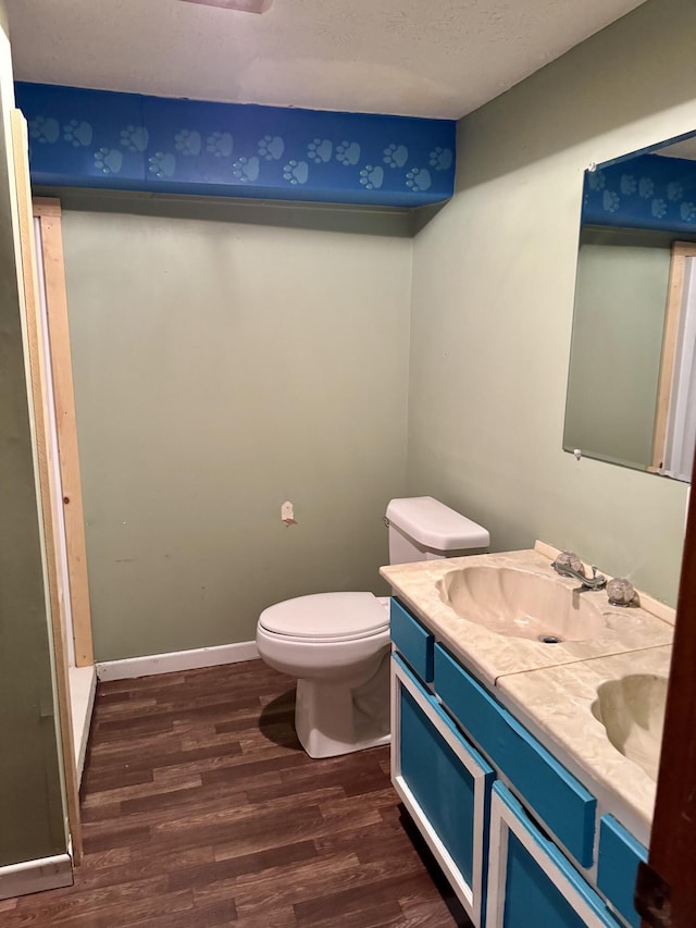 bathroom with toilet, wood finished floors, a sink, baseboards, and double vanity