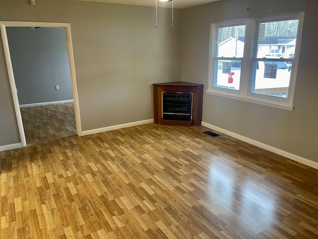 empty room featuring heating unit, a fireplace, and light hardwood / wood-style floors