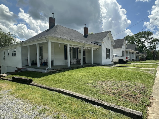 back of property featuring a porch, a lawn, a shingled roof, and a chimney