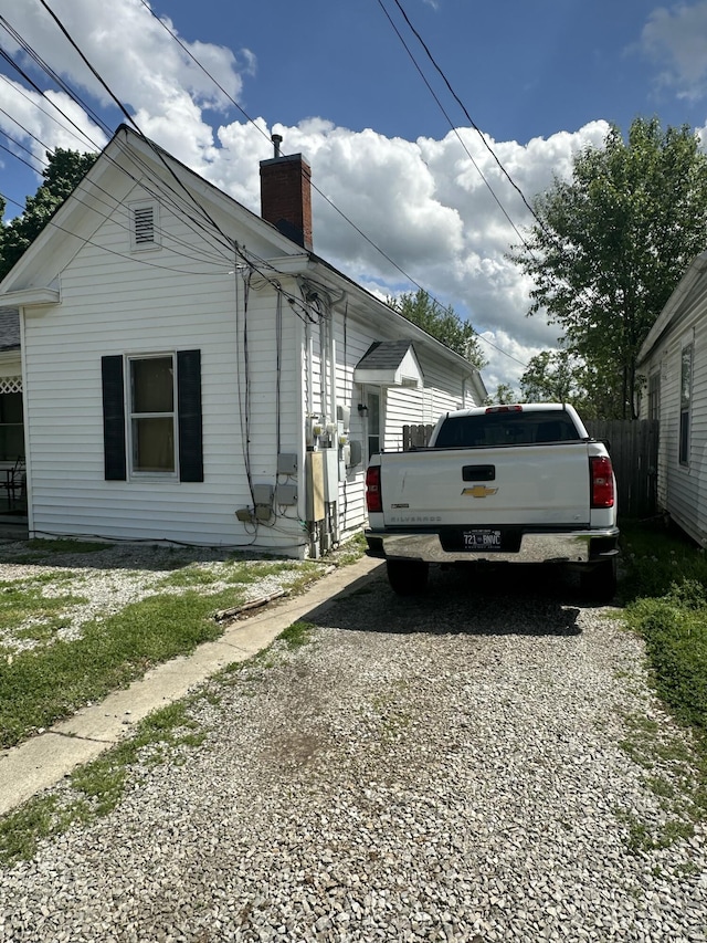 view of property exterior featuring driveway, a chimney, and fence