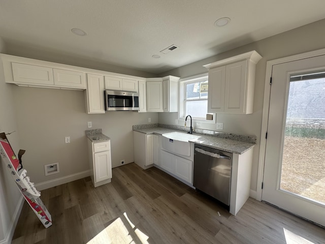 kitchen featuring white cabinets, sink, light hardwood / wood-style floors, light stone counters, and stainless steel appliances