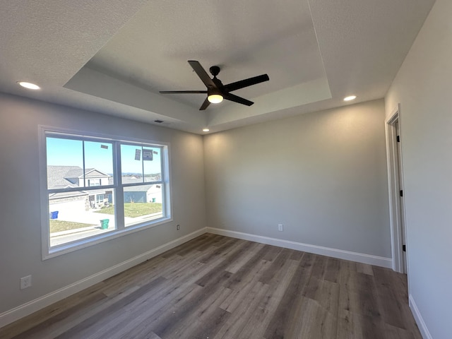 spare room featuring a tray ceiling, ceiling fan, wood-type flooring, and a textured ceiling