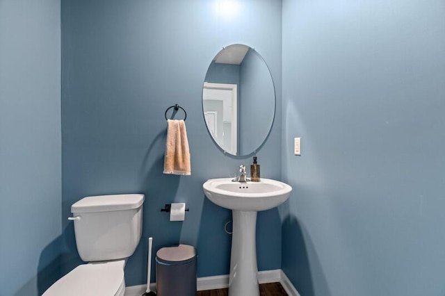 half bath with baseboards, wood finished floors, and toilet