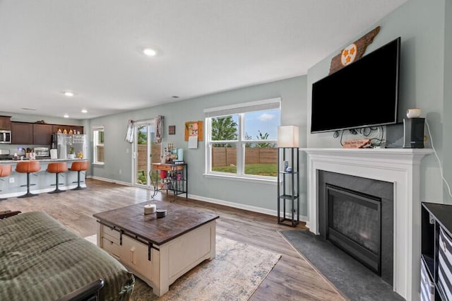 living area with light wood-type flooring, recessed lighting, a fireplace with flush hearth, and baseboards