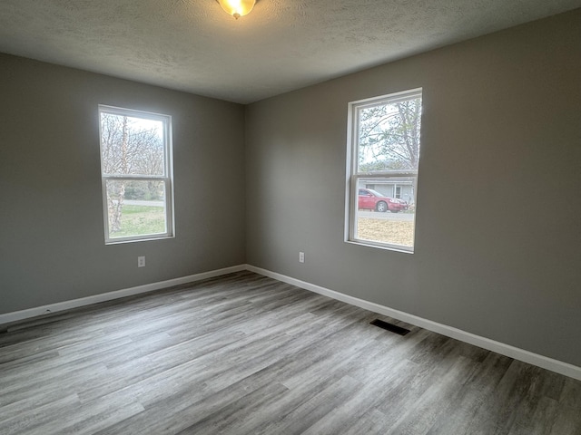 unfurnished room featuring a textured ceiling, a healthy amount of sunlight, wood finished floors, and visible vents