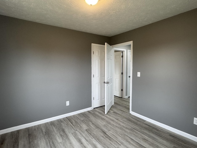 empty room with baseboards, a textured ceiling, and wood finished floors