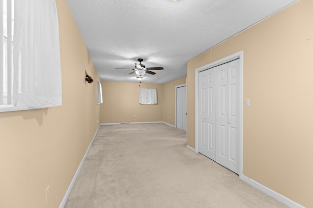 interior space featuring ceiling fan, two closets, light colored carpet, and a textured ceiling