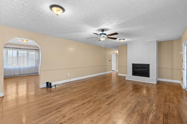 unfurnished living room featuring ceiling fan, wood-type flooring, a fireplace, and a textured ceiling