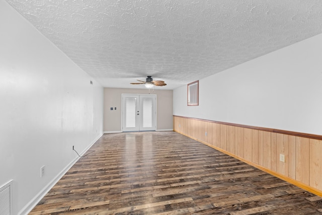 spare room featuring wood walls, ceiling fan, dark wood-type flooring, a textured ceiling, and french doors