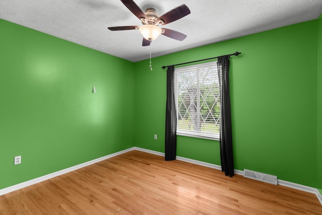 empty room featuring a ceiling fan, baseboards, visible vents, and wood finished floors