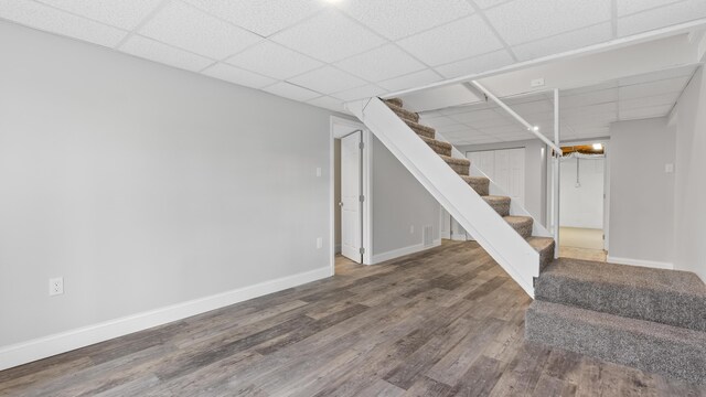 finished basement featuring baseboards, wood finished floors, a drop ceiling, and stairway