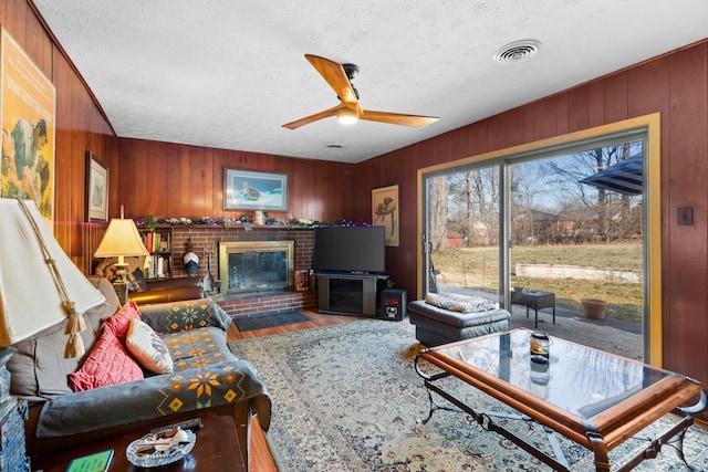 living room featuring ceiling fan, a fireplace, a textured ceiling, and wood-type flooring