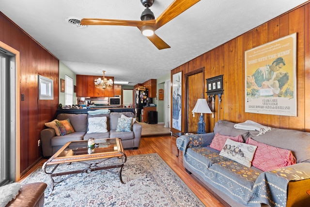 living room with wooden walls, ceiling fan with notable chandelier, and a textured ceiling