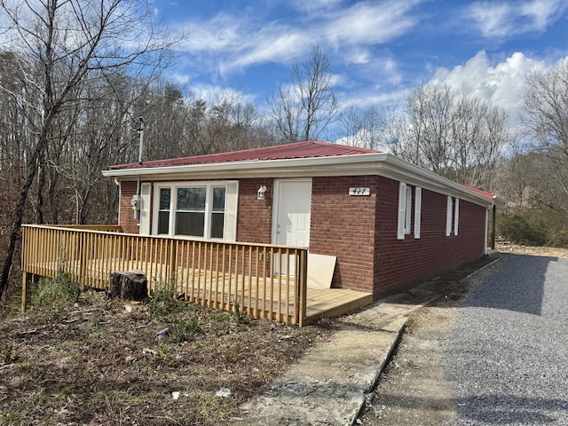 view of front of house with a deck, metal roof, brick siding, and gravel driveway