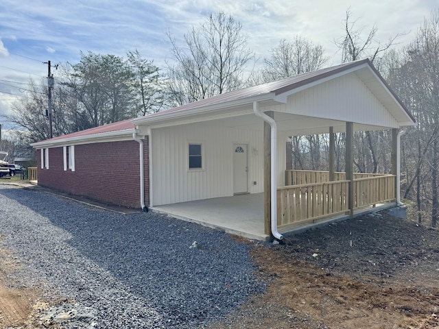 view of home's exterior featuring a carport, a patio area, gravel driveway, and brick siding