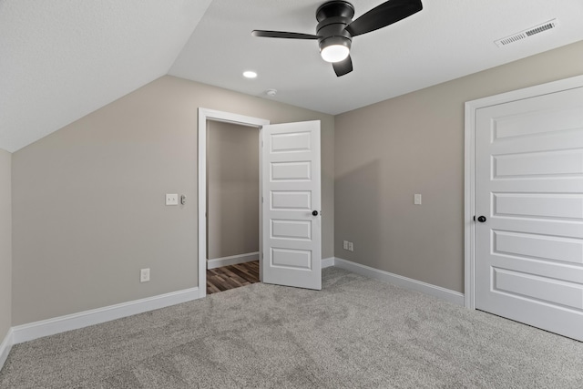 unfurnished bedroom featuring a ceiling fan, visible vents, baseboards, lofted ceiling, and carpet