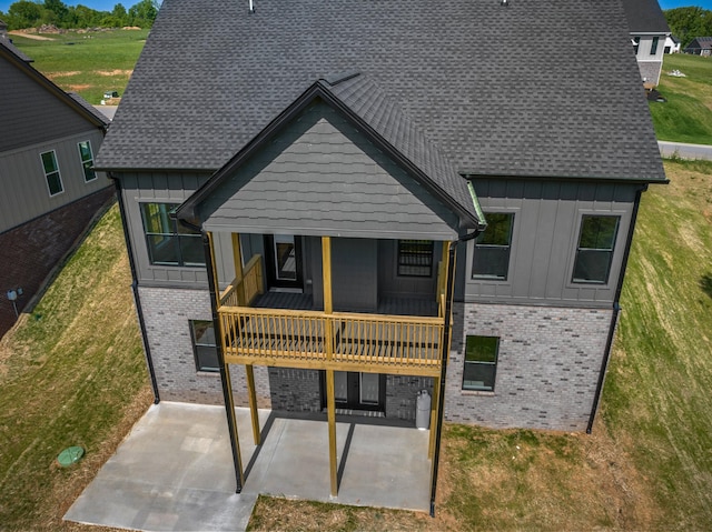 rear view of property with a lawn, board and batten siding, a patio area, and brick siding