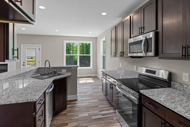 kitchen with wood finished floors, dark brown cabinets, light stone countertops, a sink, and appliances with stainless steel finishes