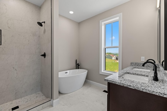 bathroom featuring marble finish floor, a freestanding tub, baseboards, tiled shower, and a sink