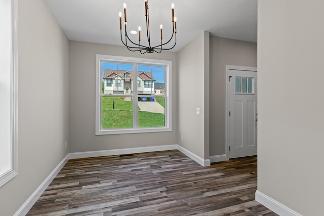 unfurnished dining area featuring baseboards, wood finished floors, and a notable chandelier