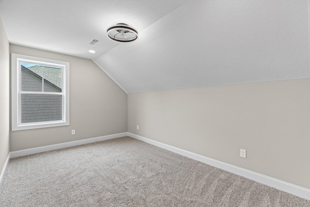 additional living space with a textured ceiling, visible vents, vaulted ceiling, baseboards, and carpet flooring
