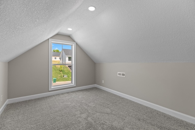 additional living space with carpet flooring, a textured ceiling, baseboards, lofted ceiling, and visible vents