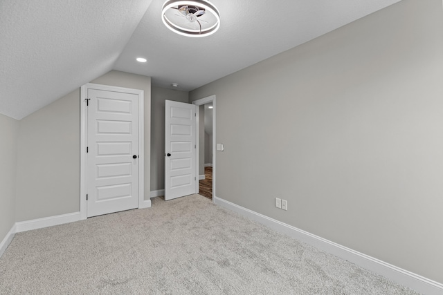unfurnished bedroom featuring baseboards, carpet flooring, a textured ceiling, and lofted ceiling