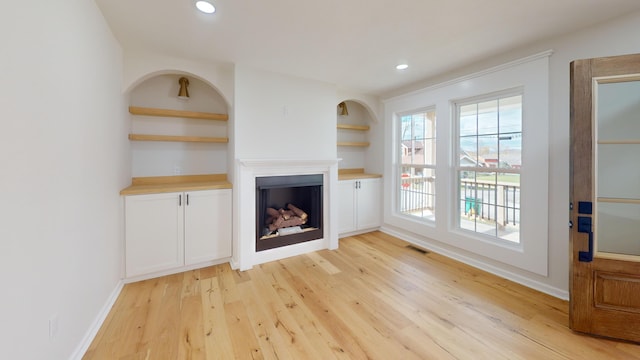 unfurnished living room with built in shelves and light hardwood / wood-style floors