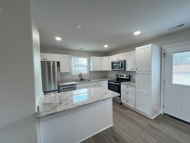 kitchen featuring light stone countertops, appliances with stainless steel finishes, sink, wood-type flooring, and white cabinets