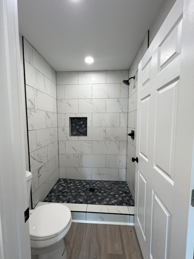 bathroom featuring hardwood / wood-style flooring, toilet, and a tile shower