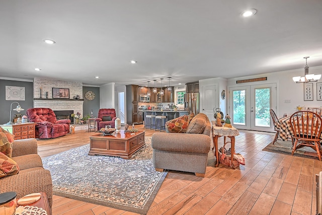 living area featuring crown molding, light wood-type flooring, an inviting chandelier, and a brick fireplace