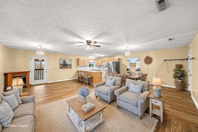 living room featuring ceiling fan, a textured ceiling, and light wood-type flooring