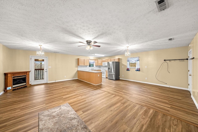 unfurnished living room with ceiling fan with notable chandelier, light hardwood / wood-style floors, and a textured ceiling