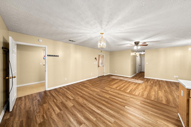 empty room with wood-type flooring, ceiling fan with notable chandelier, and a textured ceiling