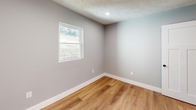 spare room with a textured ceiling, light wood-type flooring, and baseboards