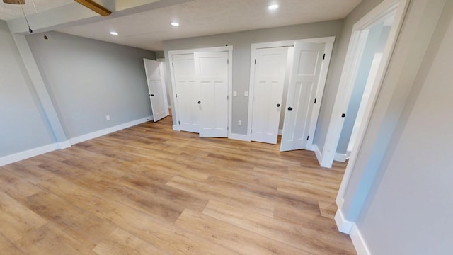 unfurnished bedroom featuring recessed lighting, light wood-style flooring, baseboards, and two closets