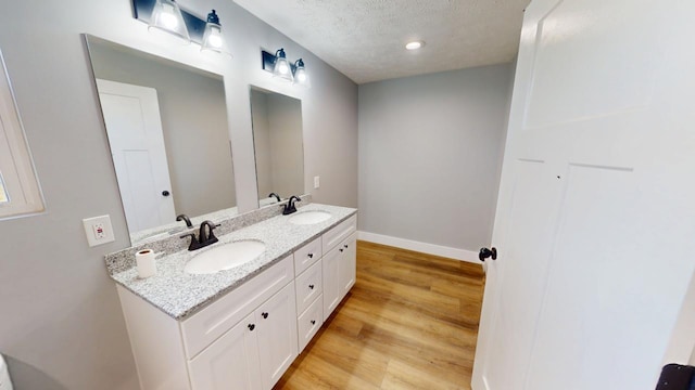 bathroom featuring a textured ceiling, wood finished floors, a sink, baseboards, and double vanity