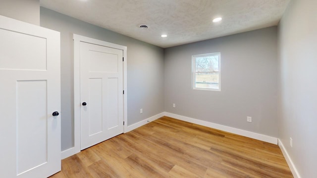 empty room featuring light wood-style floors, visible vents, a textured ceiling, and baseboards