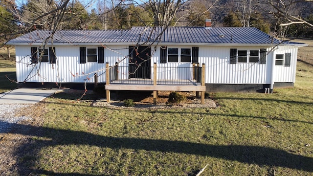 ranch-style home with metal roof, a chimney, a front yard, and a wooden deck